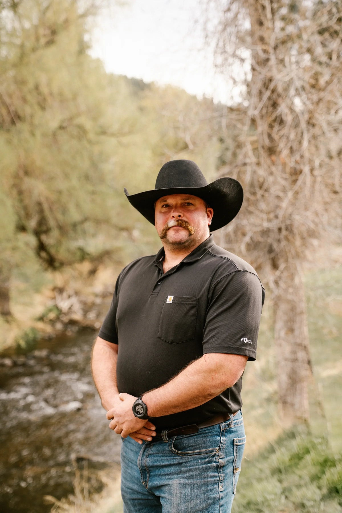Evan Jeffries standing by a creek at the ranch in a black cowboy hat
