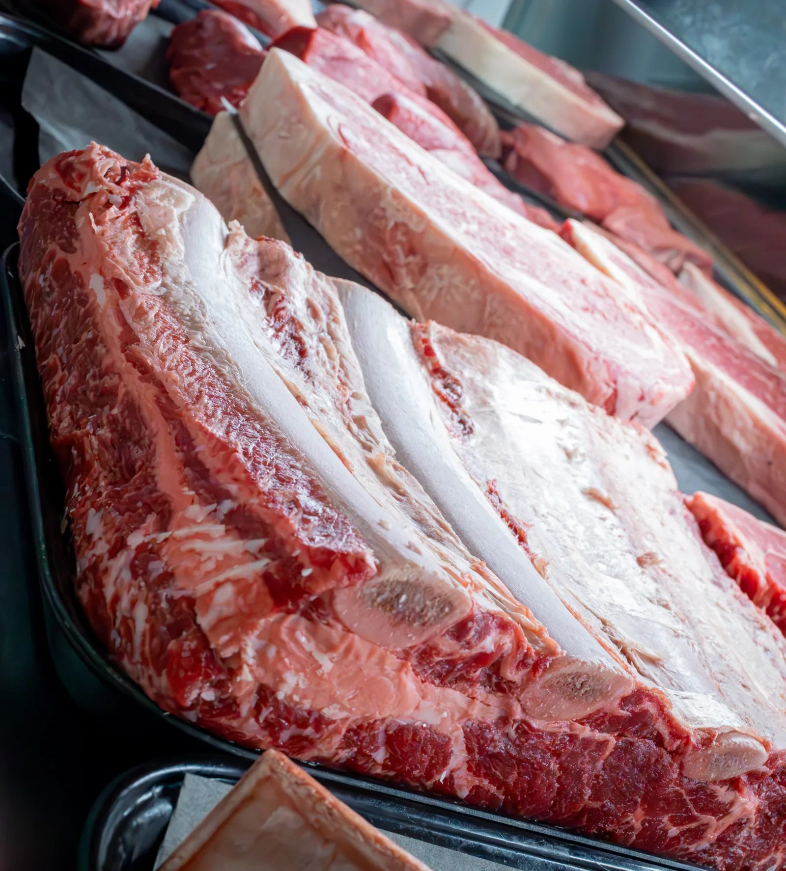 Close-up of several rows of raw beef with dense, heavy marbling laid out side by side in a butcher case.