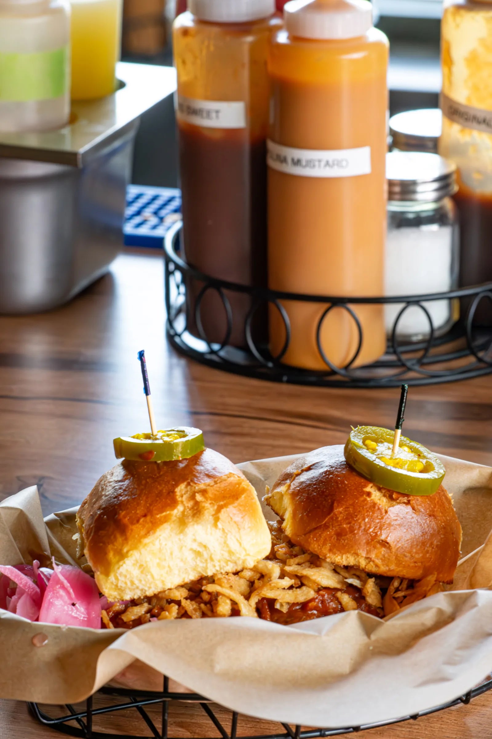 Two BBQ sliders on brioche buns topped with candied jalapeno picks and piled with crispy fried onion straws.