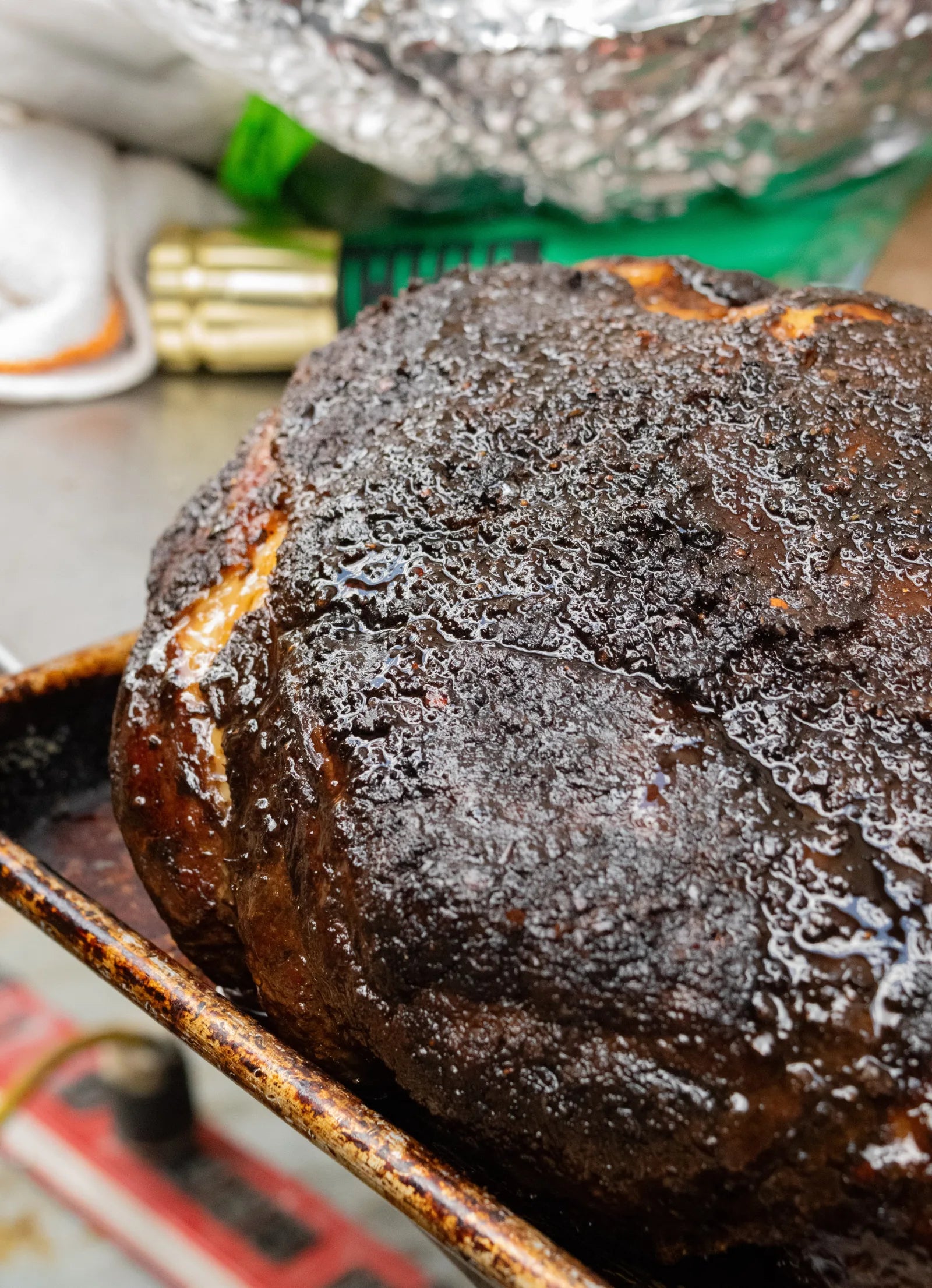 Close-up of a whole smoked brisket with a thick, dark, glistening peppery bark, resting on a well-used metal prep tray.
