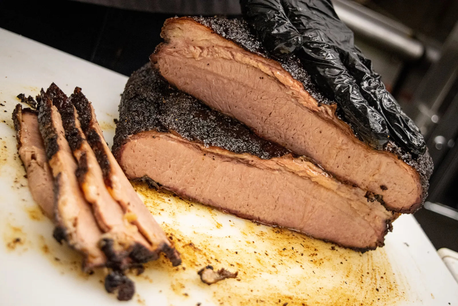 Smoked brisket with a dark peppery bark, partially sliced into several pieces stacked on a white cutting board.
