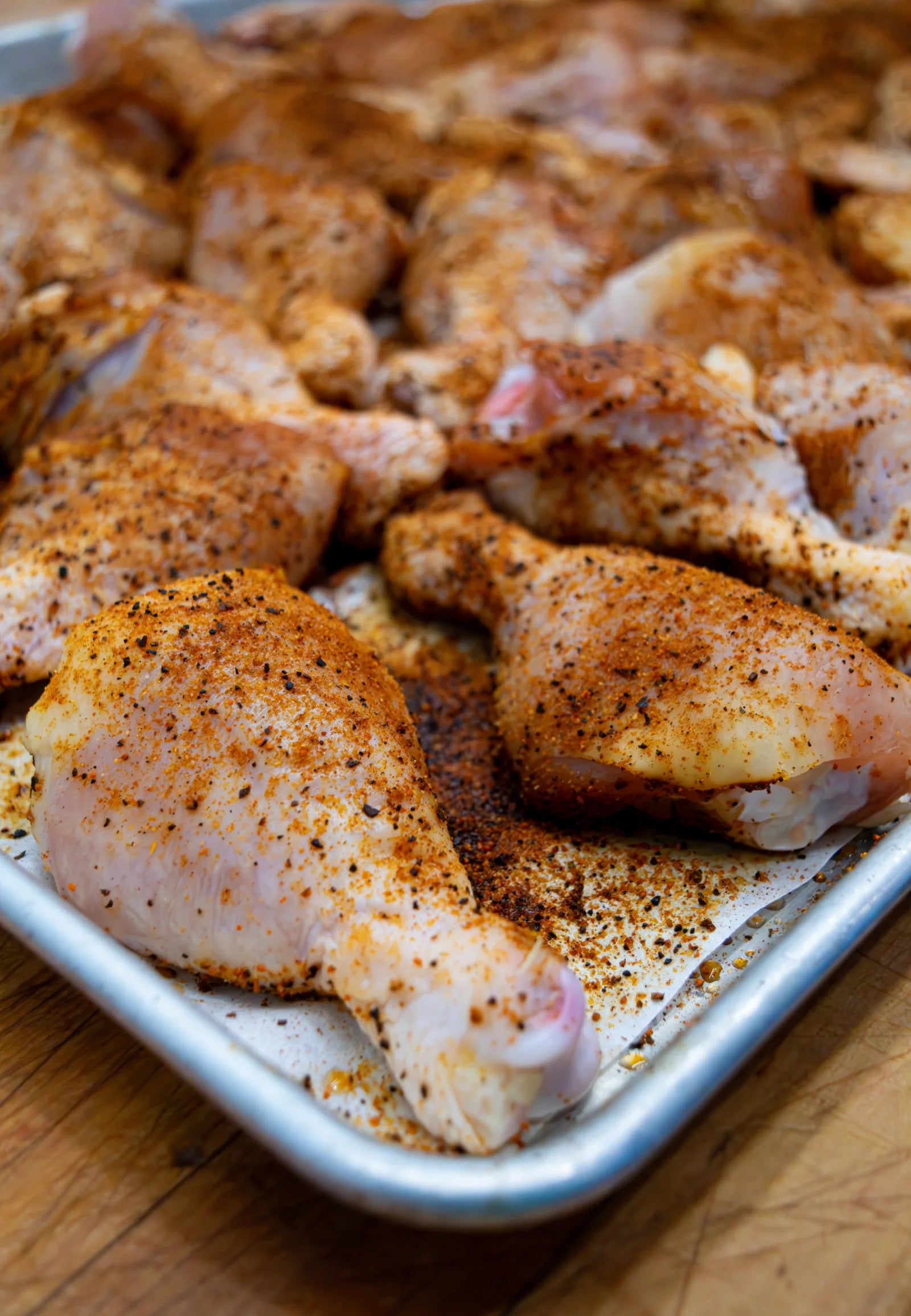 Close-up of raw chicken leg quarters generously coated in a coarse orange and black spice rub.