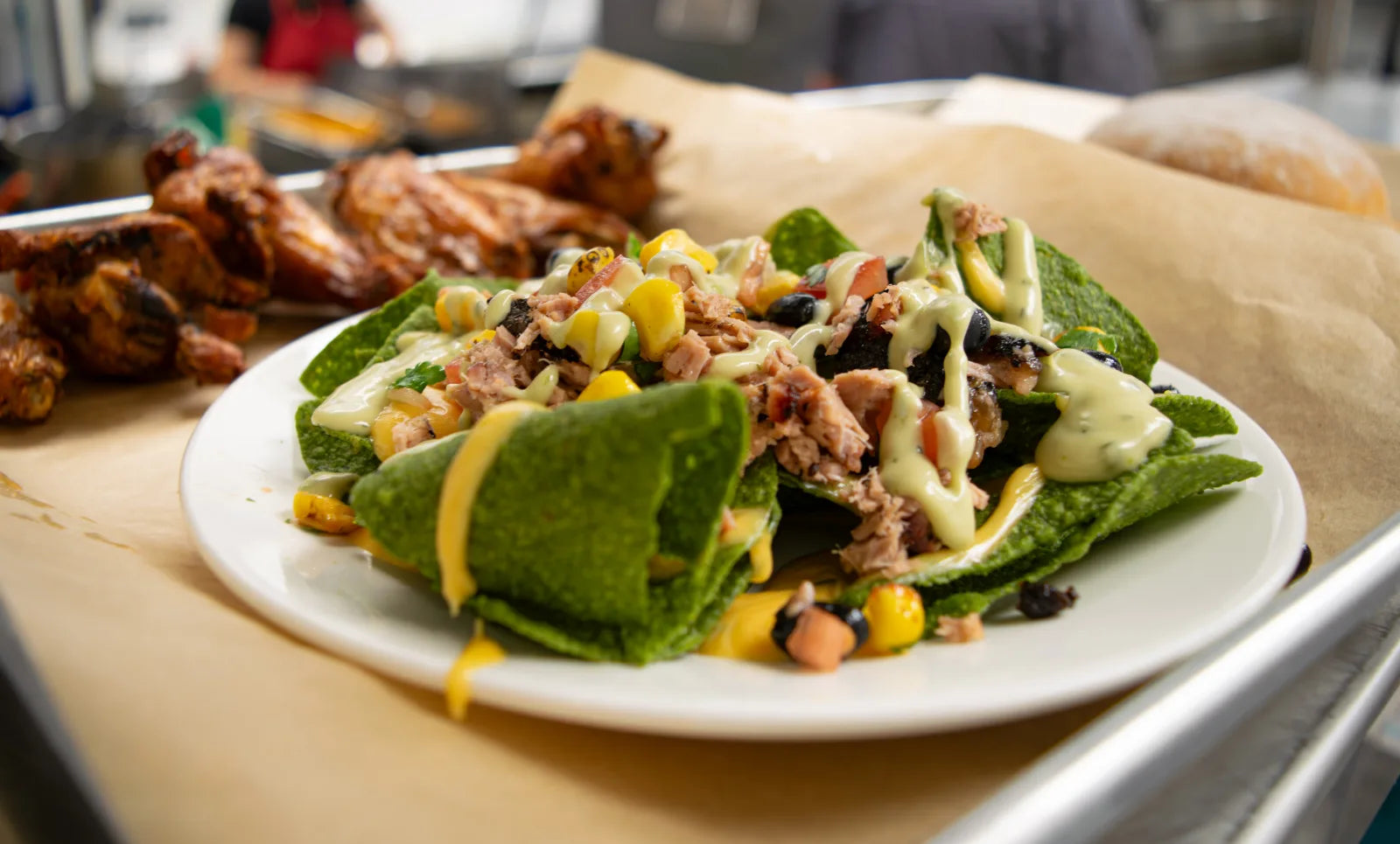 A plate of loaded BBQ nachos with pulled meat, corn, black beans, and avocado crema