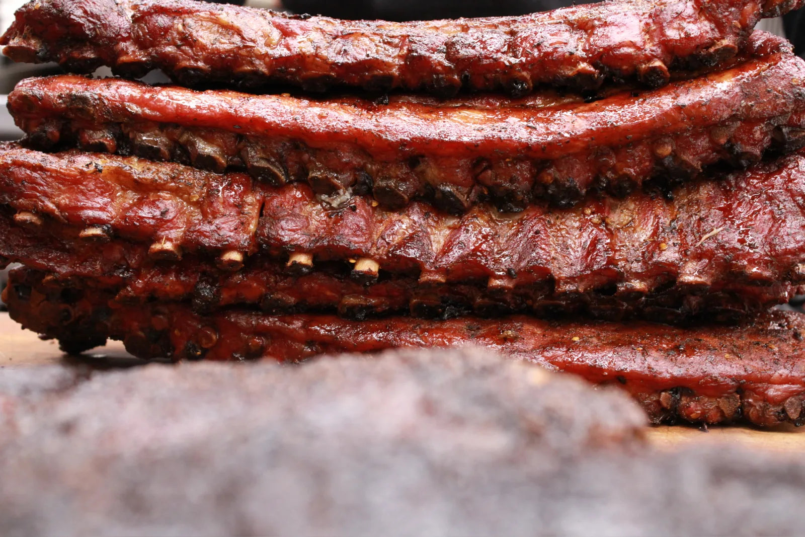 A stack of smoked beef ribs with dark peppery bark and rib bones exposed at the ends.