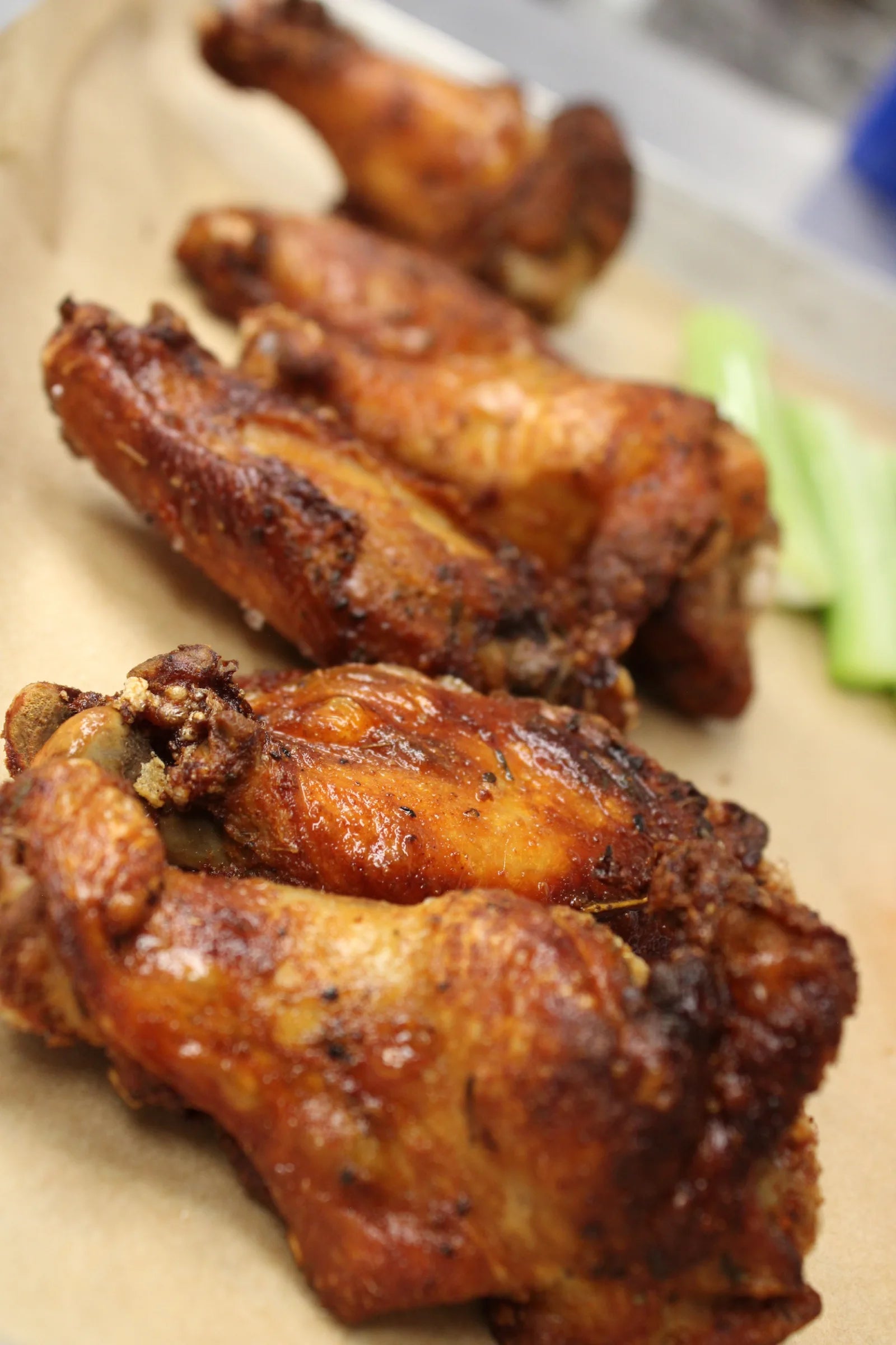 Glossy glazed chicken wings piled on parchment paper with celery sticks in the background.