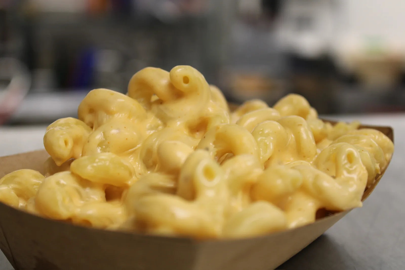 A close-up of a paper serving boat piled high with creamy macaroni and cheese.