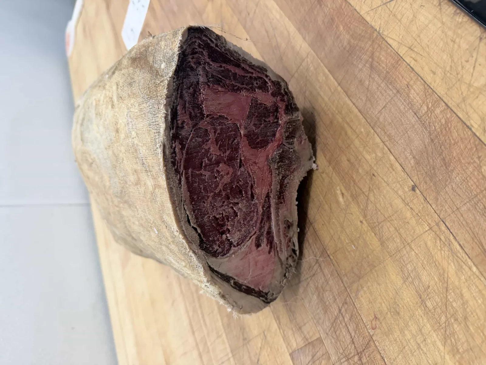 A cheesecloth-wrapped beef roast, miso dry-aged for 60 days, cut open to reveal a dark aged crust and deep red interior.