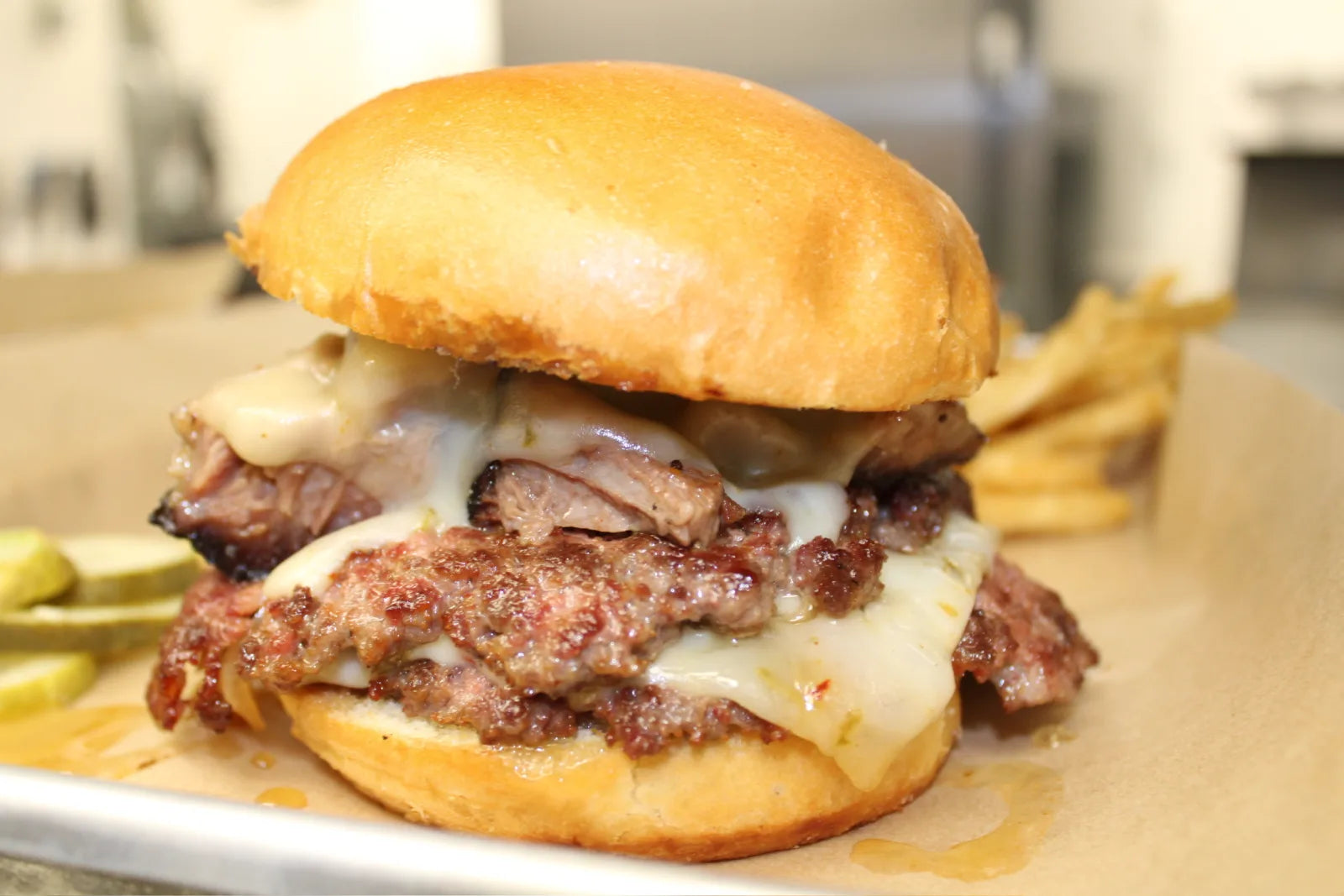 A stacked burger with two smashed beef patties, chopped brisket, melted white cheese, and pickled jalapenos on a toasted bun.