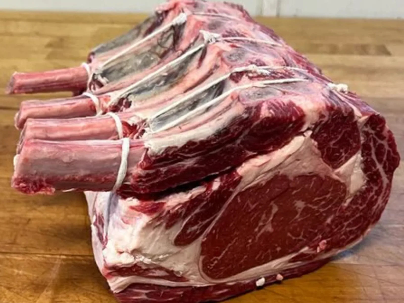 A frenched, dry-aged bone-in rib roast with heavy marbling on a wooden butcher block.