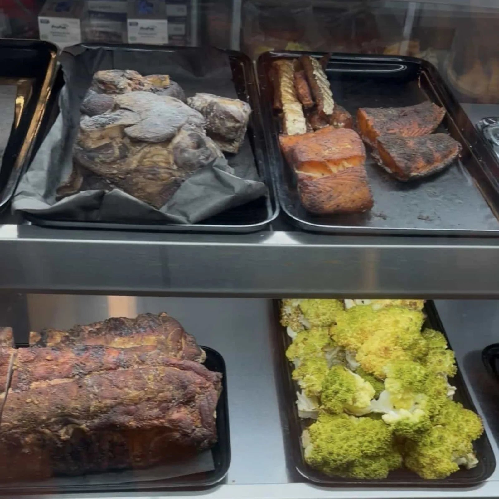 Trays of smoked prime rib and glazed salmon in the display case, with roasted vegetables below.