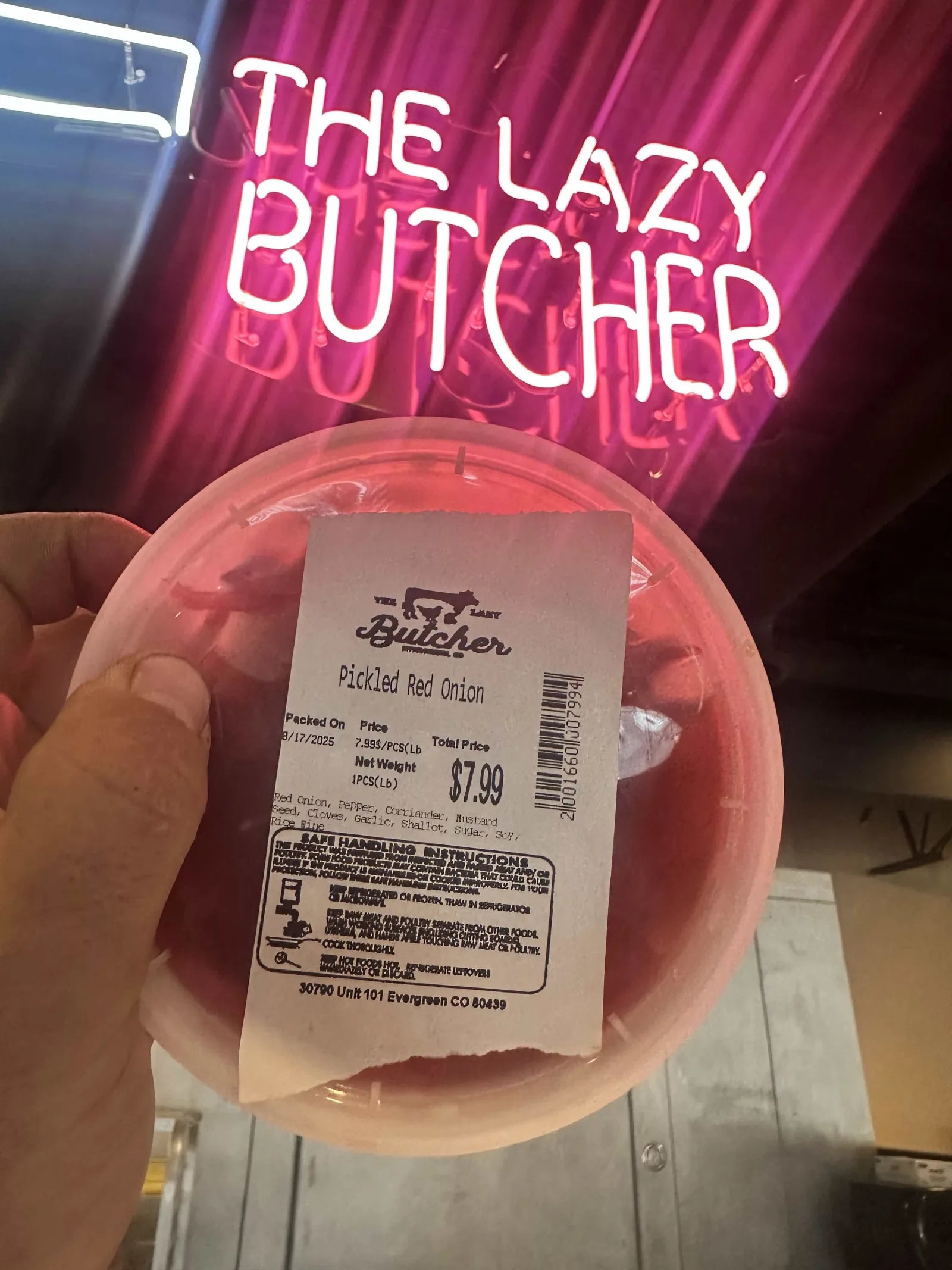 A container of house pickled red onion under the Lazy Butcher neon sign