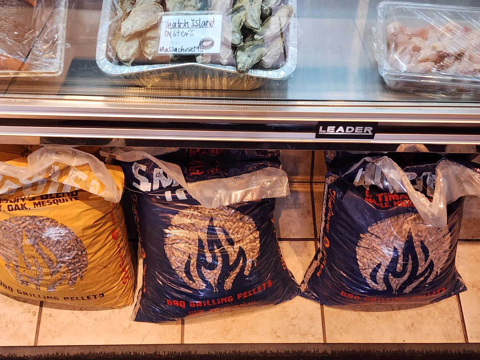 Bags of BBQ grilling pellets in hickory, oak, mesquite, and maple blends below the seafood case
